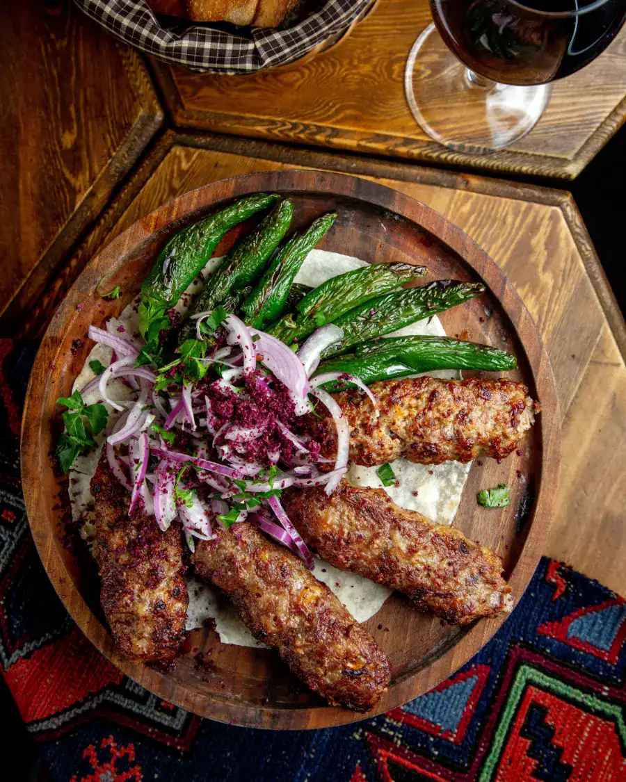 Grilled kofta kebabs served with roasted green peppers and sumac onions on a wooden platter
