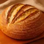 Whole loaf of freshly baked San Francisco sourdough bread with a golden crust on a wooden board.