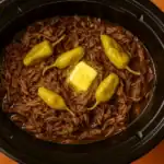 Shredded Mississippi pot roast in a slow cooker with butter and pepperoncini peppers