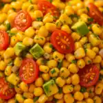 Close-up of corn salad with cherry tomatoes, avocado, red onion, and chopped herbs