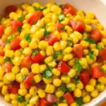 Close-up of corn salad with diced tomatoes, red onion, and chopped herbs in a white bowl