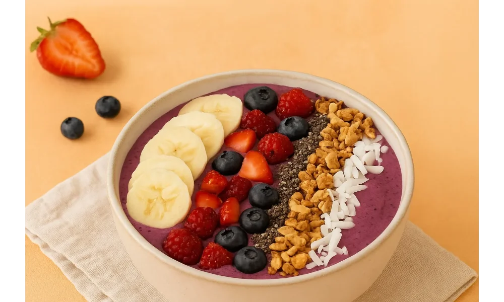 Smoothie bowl topped with banana slices, berries, granola, chia seeds, and coconut flakes on a warm background