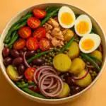 Authentic Niçoise salad in a ceramic bowl with tuna, eggs, green beans, potatoes, tomatoes, olives, onions, and capers