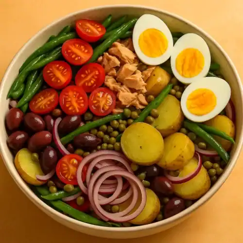 Authentic Niçoise salad in a ceramic bowl with tuna, eggs, green beans, potatoes, tomatoes, olives, onions, and capers