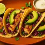 Grilled Mahi Mahi tacos topped with avocado and purple cabbage slaw on a warm-toned plate.