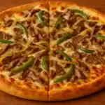 Philly cheesesteak pizza topped with sliced steak, green bell peppers, and onions on a golden crust