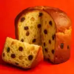 Sliced panettone with raisins and orange peel against a vibrant red background
