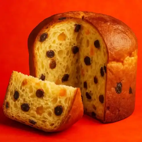 Sliced panettone with raisins and orange peel against a vibrant red background