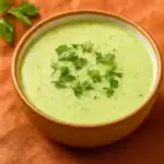 Chilled zucchini soup with fresh herbs in a brown ceramic bowl