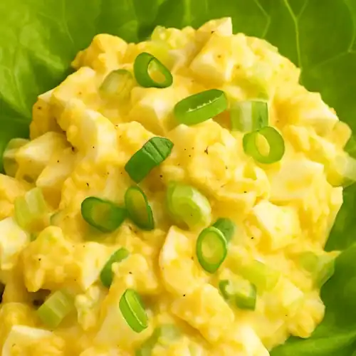 Close-up of creamy classic egg salad topped with chopped green onions, served in a fresh lettuce leaf.