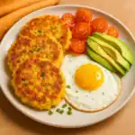 Crispy corn cakes served with fried egg, avocado slices, and cherry tomatoes on a breakfast plate