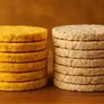 Two neat stacks of corn cakes and rice cakes side by side on a wooden surface with a warm brown background.