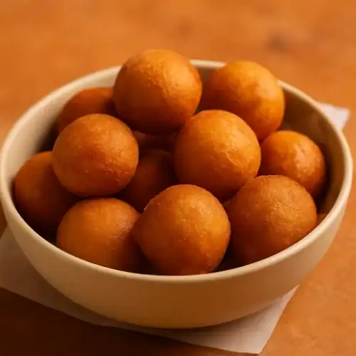 Golden homemade donut holes in a cream-colored bowl on a warm-toned surface