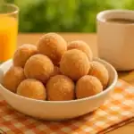 A bowl of sugar-coated 3-ingredient donut holes served with coffee and orange juice on a summer breakfast table.