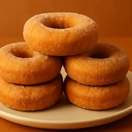Stack of golden-brown buttermilk donuts on a beige plate with a warm orange background.