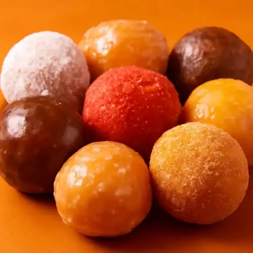 A colorful close-up of assorted Dunkin’ donut holes on a warm orange background.