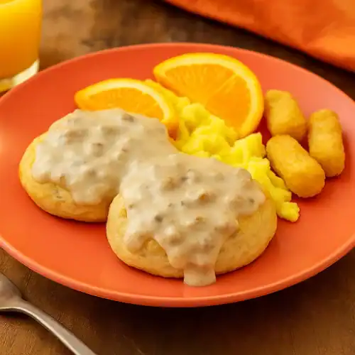 Biscuits with sausage gravy served with scrambled eggs, tater tots, and orange slices on a breakfast plate