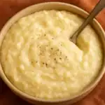 Close-up of creamy potato grits in a bowl with a spoon and a sprinkle of black pepper