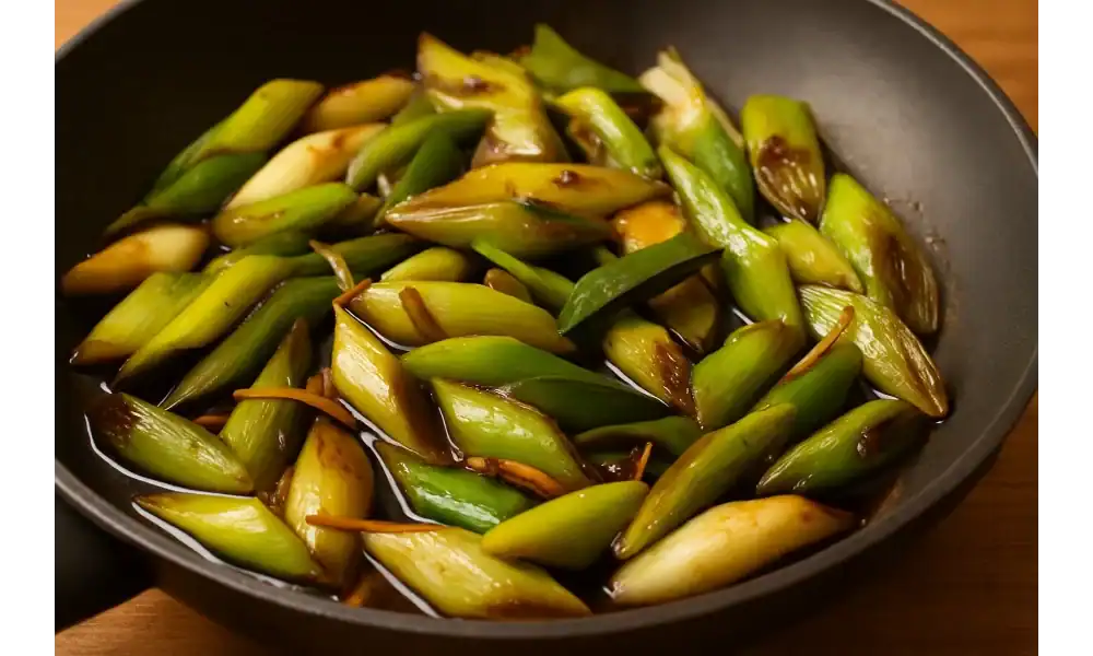 Stir-fried leeks with soy sauce and ginger in a black skillet on a wooden surface. it is one of Easy and Delicious Leek Recipes that you wanna try!