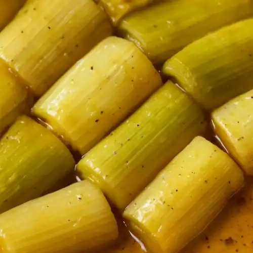 Close-up of tender braised leeks in a golden sauce with seasoning