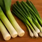 Fresh leeks and green onions side by side on a wooden surface