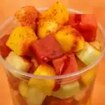 Close-up of a Mexican fruit cup filled with mango, watermelon, cucumber, and jicama, topped with chili powder and chamoy.