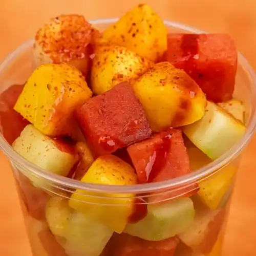 Close-up of a Mexican fruit cup filled with mango, watermelon, cucumber, and jicama, topped with chili powder and chamoy.