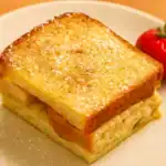 Close-up of a golden slice of pain perdu on a plate, lightly dusted with powdered sugar and served with a fresh strawberry