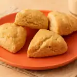 Golden-brown vegan scones served on a coral plate with a glass of oat milk in the background