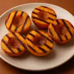 Grilled peach halves with caramelized brown sugar and cinnamon served on a ceramic plate.