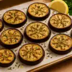 Freshly roasted Mediterranean eggplant slices on a parchment-lined tray, garnished with herbs and served with lemon and parsley.