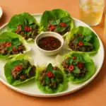 Vietnamese beef lettuce wraps with ground beef, herbs, chili, and dipping sauce served with iced tea on a dinner table.