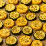 Roasted zucchini and yellow squash slices on a baking sheet with herbs and seasoning.