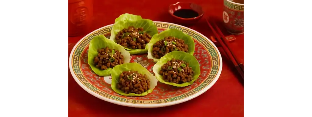 Chinese beef lettuce wraps served on a traditional patterned plate with scallions and sesame seeds, styled with chopsticks and soy sauce on a red Chinese table setting.