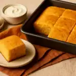 Fluffy squares of Jiffy cornbread with sour cream served on a white plate with warm brunch sides.
