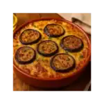 Close-up of baked moussaka topped with roasted eggplant slices in a red dish.