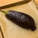 Roasted whole eggplant on a parchment-lined baking tray, fresh from the oven.