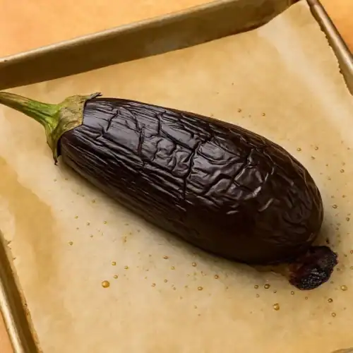 Roasted whole eggplant on a parchment-lined baking tray, fresh from the oven.