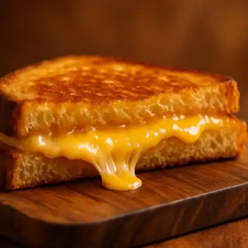 Golden-brown grilled cheese on a wooden board with melted cheddar stretching from the center, warm background.