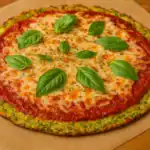 Whole grated zucchini pizza with tomato sauce, melted cheese, and fresh basil leaves on a wooden table.