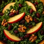 Close-up of kale apple walnut cranberry salad with crisp apple slices, dried cranberries, and toasted walnuts on fresh green kale leaves, lightly dressed in maple Dijon vinaigrette.