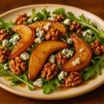 A plate of warm caramelised pear and blue cheese salad with toasted walnuts and arugula, drizzled with honey balsamic dressing.