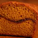 Close-up of a moist slice of pumpkin bread with a visible cinnamon swirl, warm golden crumb, and cozy fall tones.