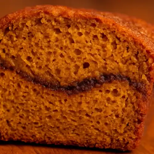 Close-up of a moist slice of pumpkin bread with a visible cinnamon swirl, warm golden crumb, and cozy fall tones.