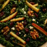 Close-up of kale apple balsamic salad with crisp apple sticks, toasted walnuts, dried cranberries, and crumbled feta in a tangy vinaigrette.