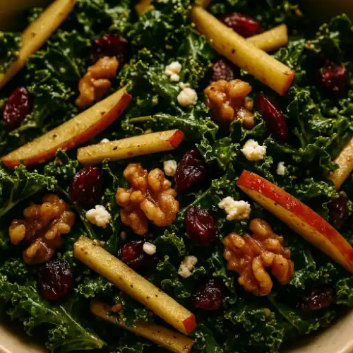 Close-up of kale apple balsamic salad with crisp apple sticks, toasted walnuts, dried cranberries, and crumbled feta in a tangy vinaigrette.