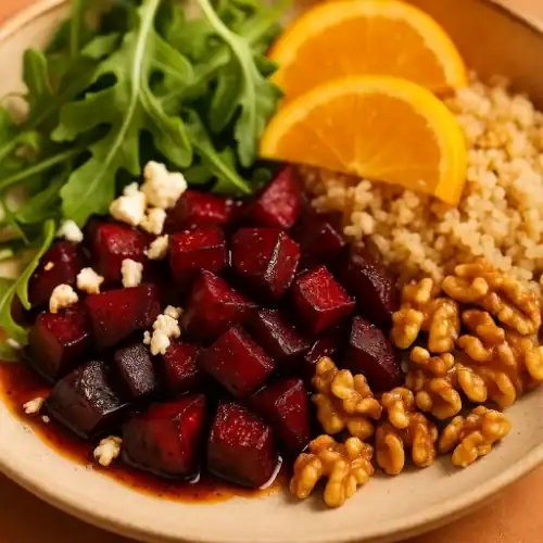 Close-up of roasted beet cubes served with quinoa, arugula, orange slices, walnuts, and crumbled feta on a beige plate.