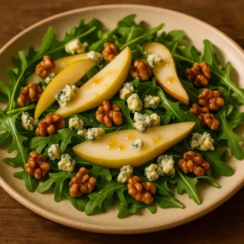 Two plates of pear and blue cheese salad with arugula, walnuts, and honey vinaigrette served on a wooden table with candles and glasses of juice for a cozy dinner for two.