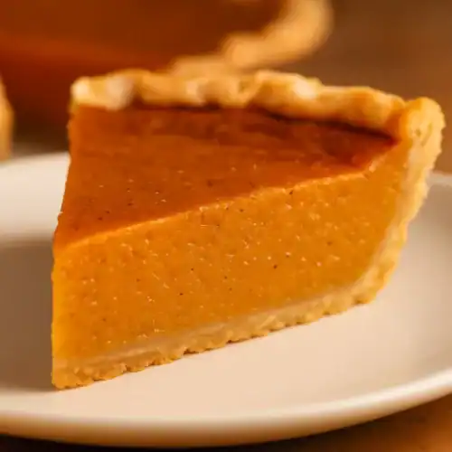 Close-up of a single slice of sweet potato pie on a white plate showing its creamy orange filling and flaky golden crust.