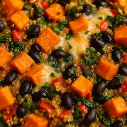 Close-up of a sweet potato quinoa bake with black beans, red peppers, and spinach, topped with melted cheese and herbs.